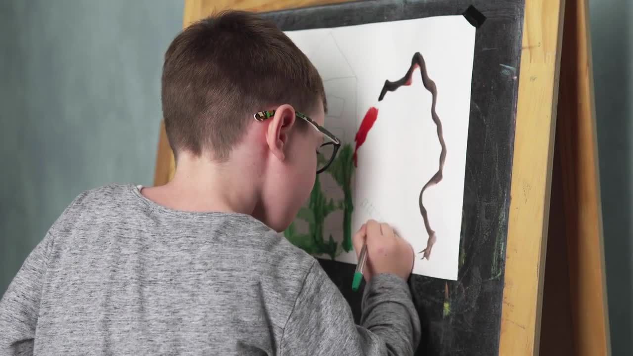 戴眼镜的小男孩在画架上画画视频
