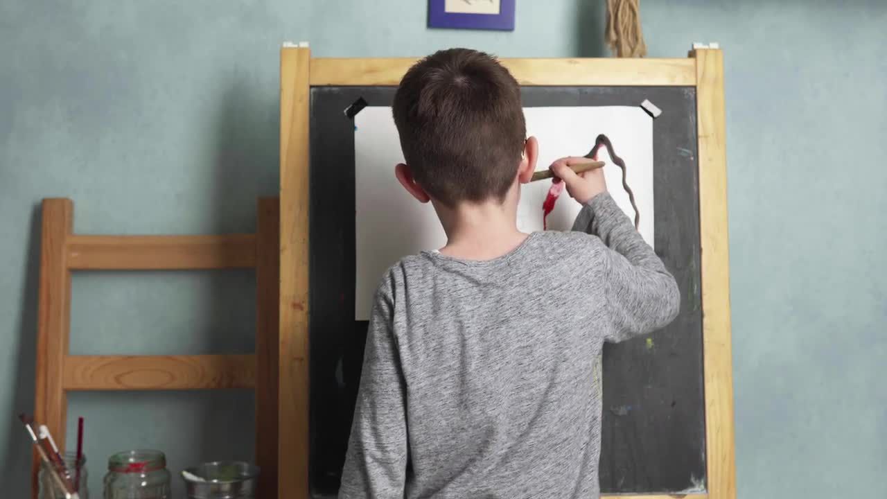 小男孩站在艺术室画架上用水彩绘画视频