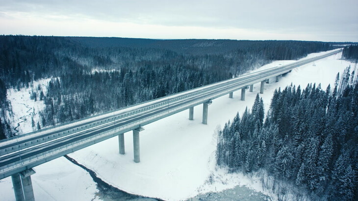 空中实拍在白雪皑皑的森林中行驶在桥上的汽车